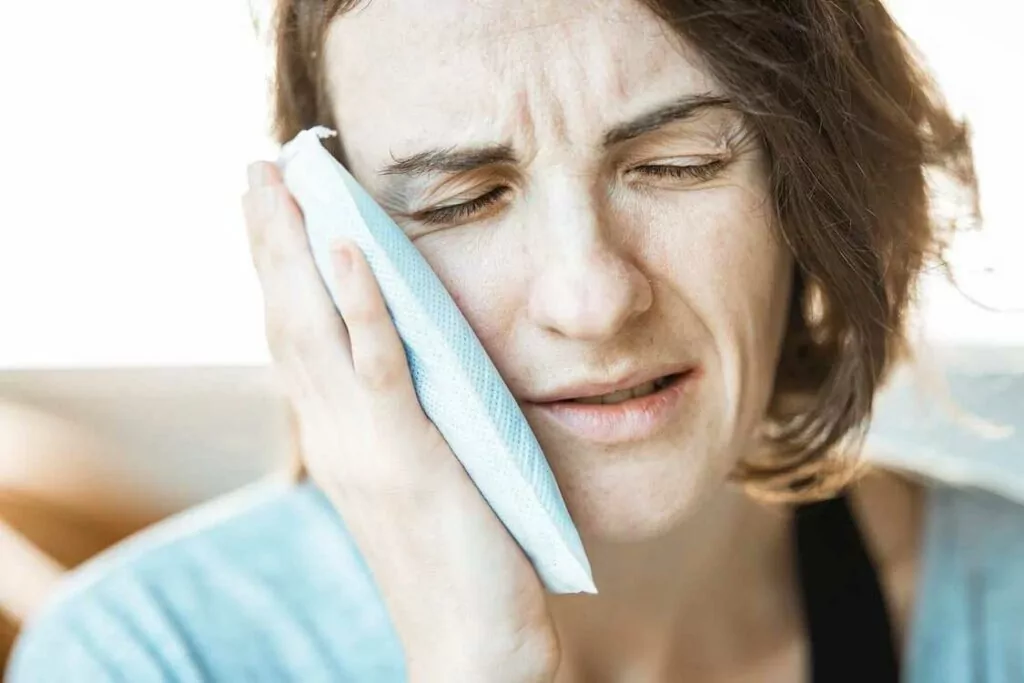 Woman with ice pack on jaw from dental emergency in Boulder