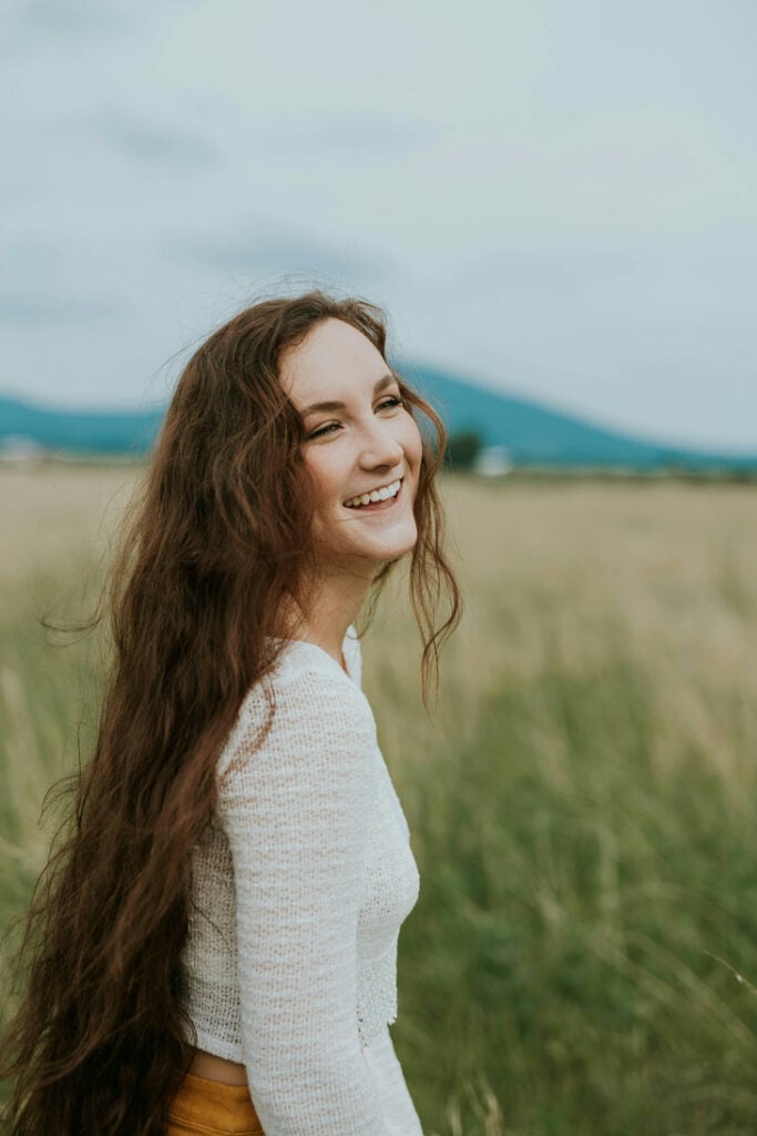 Smiling girl with straight white teeth in a field with mountain background in Colorado